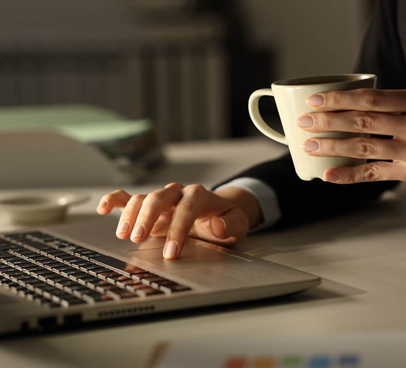 Close up of business woman hands with laptop holding coffee cup at night in the office