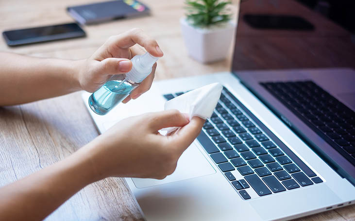 Woman cleaning laptop and smartphone by wet wipes tissue and alcohol disinfectant on workplace during work at home, protection coronavirus (Covid-19) infection  New Normal and Clean surface concept